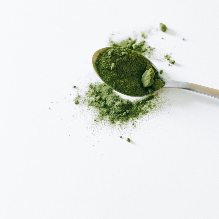 Top view of organic matcha powder on a silver spoon with a white background.