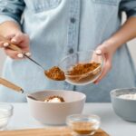Close-up of hands measuring cocoa powder for home baking preparation.